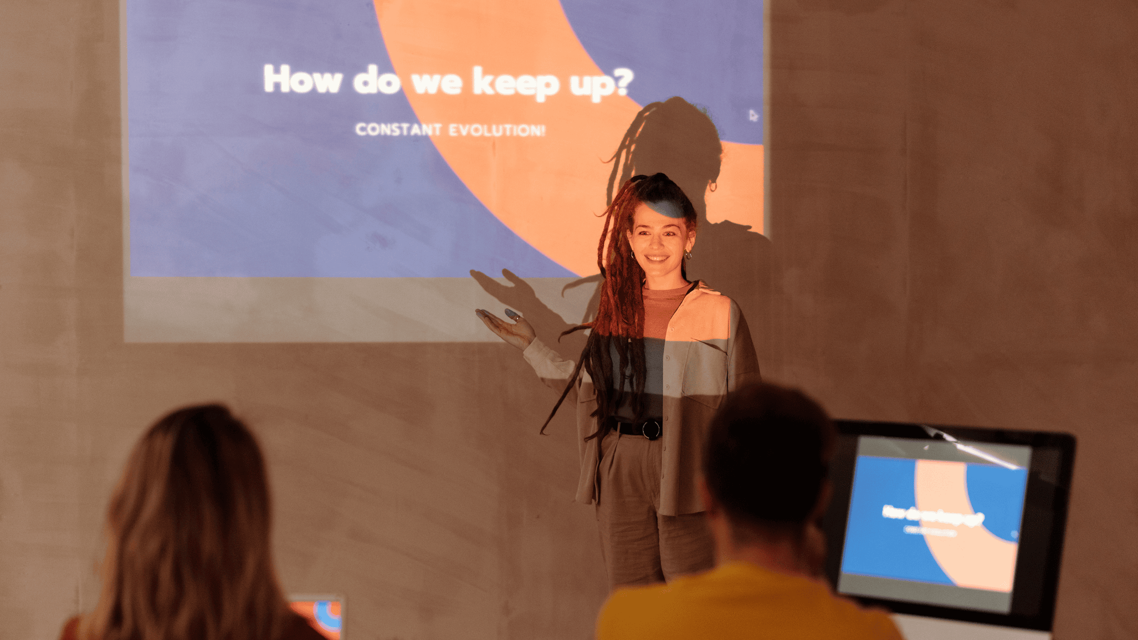 A woman presenting a live product demo on a projector while an engaged audience watches.