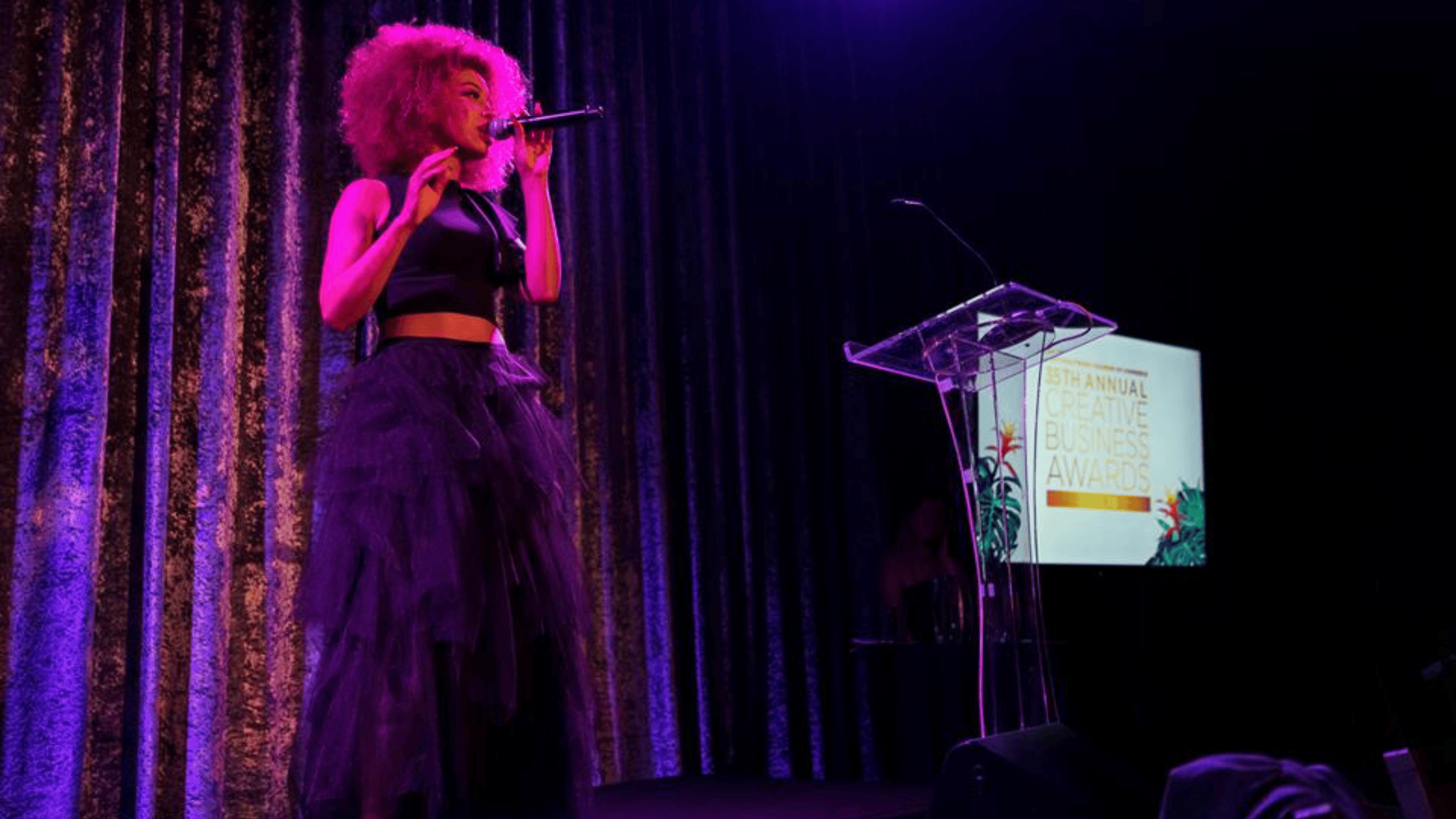 Electrifying Award Show Performance A female singer performing live at an award show, illuminated by pink and purple stage lighting, holding a microphone.