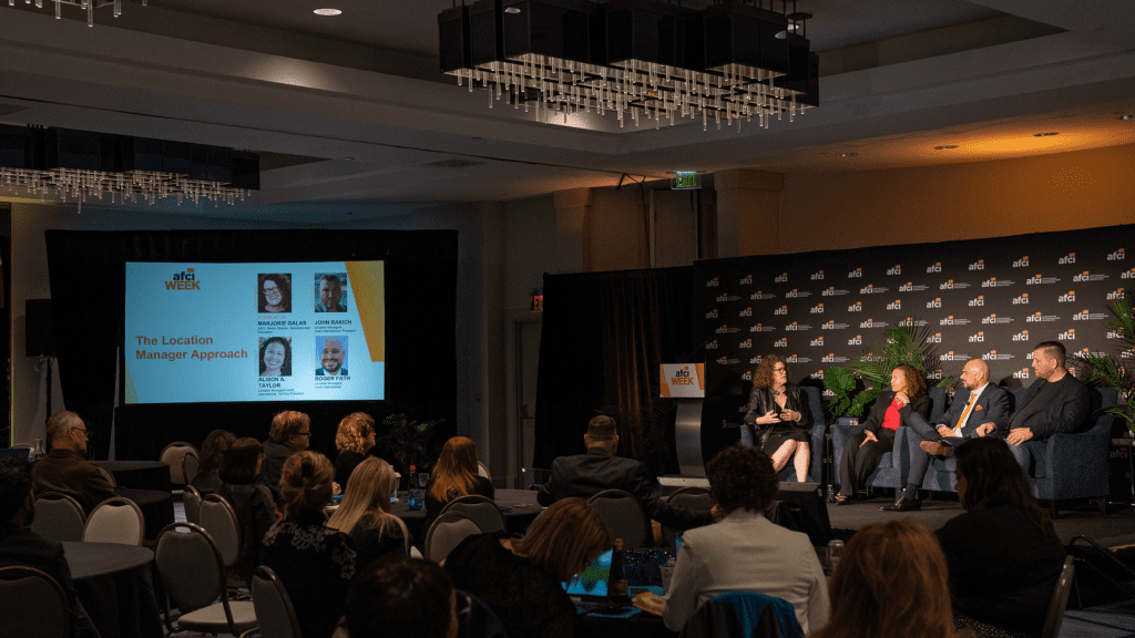 Speaker panel at AFCI Week with a moderator on stage discussing 'The Location Manager Approach' with industry experts.
