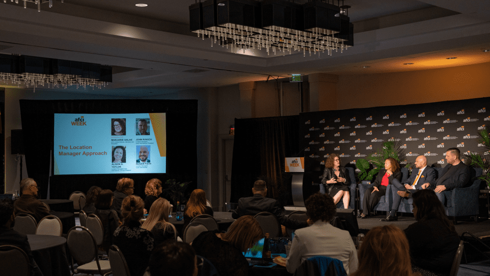 Panel discussion on stage at a film industry conference, with a seated audience.